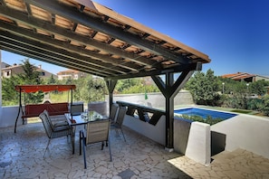 An outdoor patio with a table and chairs, a pergola, and a pool.