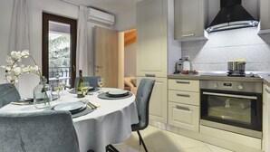 A modern kitchen with white cabinets, a black range hood, and a dining area with a table set for two. - Magnificent villa with private pool, outdoor kitchen with barbecue (Divšici)