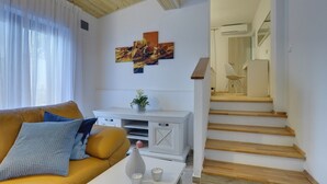 A modern living room with a yellow sofa, a white coffee table, and a painting on the wall. A staircase leads to an upper floor. - Magnificent villa with private pool, outdoor kitchen with barbecue (Divšici)