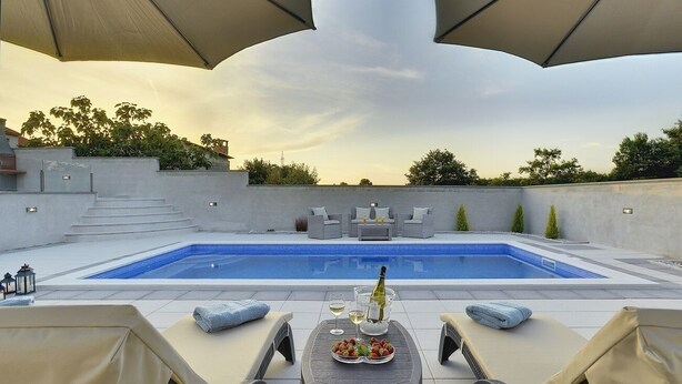 A rooftop pool area with lounge chairs, a table with a bottle and glasses, and a clear view of the pool. - Magnificent villa with private pool, outdoor kitchen with barbecue (Divšici)
