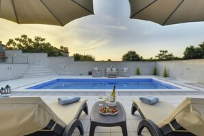 Área de piscina en la azotea con sillones reclinables, una mesa con una botella y vasos, y una vista despejada de la piscina.