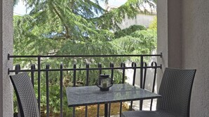 A balcony with a table and two chairs, a decorative lantern, and a view of trees and a building. - Magnificent villa with private pool, outdoor kitchen with barbecue (Divšici)