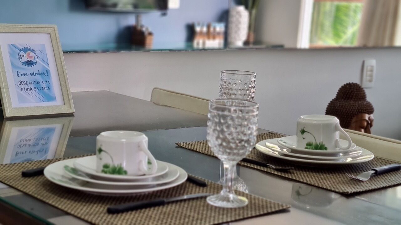 Une table à manger dressée avec deux tasses et sous-tasses blanches, un verre transparent et une statue de Bouddha.