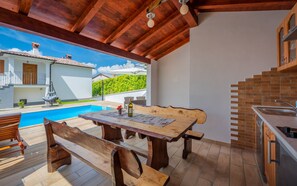 A wooden dining table with benches, a pool, and a kitchen area with a brick backsplash. - Sunny villa with private pool, sun loungers, outdoor shower (Lindar)