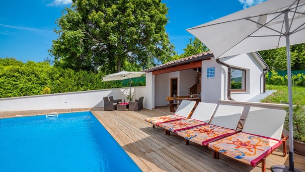 Zona junto a la piscina con sillones de descanso, una terraza de madera y una pequeña barra.