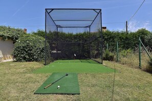 Un campo de mini golf con recinto de malla, césped de putting y un mástil con bandera.
