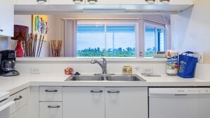 A modern kitchen with white cabinets, a stainless steel sink, and a window with a view of greenery. - Sandy Pointe 210 · Mangrove & Bay View · Pool (Holmes Beach)