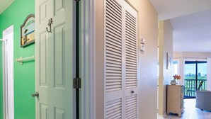 A hallway with a green wall, a white door, and a white closet with louvered doors. - Sandy Pointe 210 · Mangrove & Bay View · Pool (Holmes Beach)