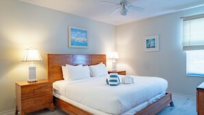 A bedroom with a wooden bed, two bedside tables with lamps, a ceiling fan, and two framed pictures on the walls. - Sandy Pointe 210 · Mangrove & Bay View · Pool (Holmes Beach)