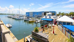 Un puerto deportivo con barcos amarrados, un edificio azul y una zona cubierta con asientos.