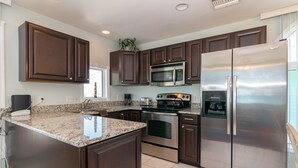 Una cocina moderna con armarios de madera oscura, electrodomésticos de acero inoxidable, encimeras de granito y horno integrado.