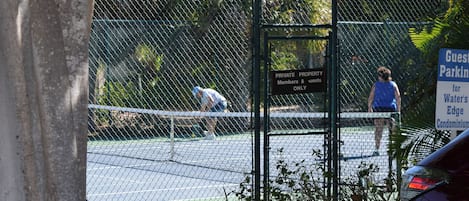 Un court de tennis entouré d’une clôture grillagée, avec un panneau indiquant qu’il s’agit d’une propriété privée réservée aux membres et à leurs invités.
