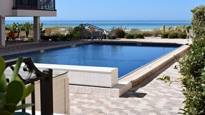 A swimming pool with a view of the ocean, surrounded by lounge chairs and a building with balconies.