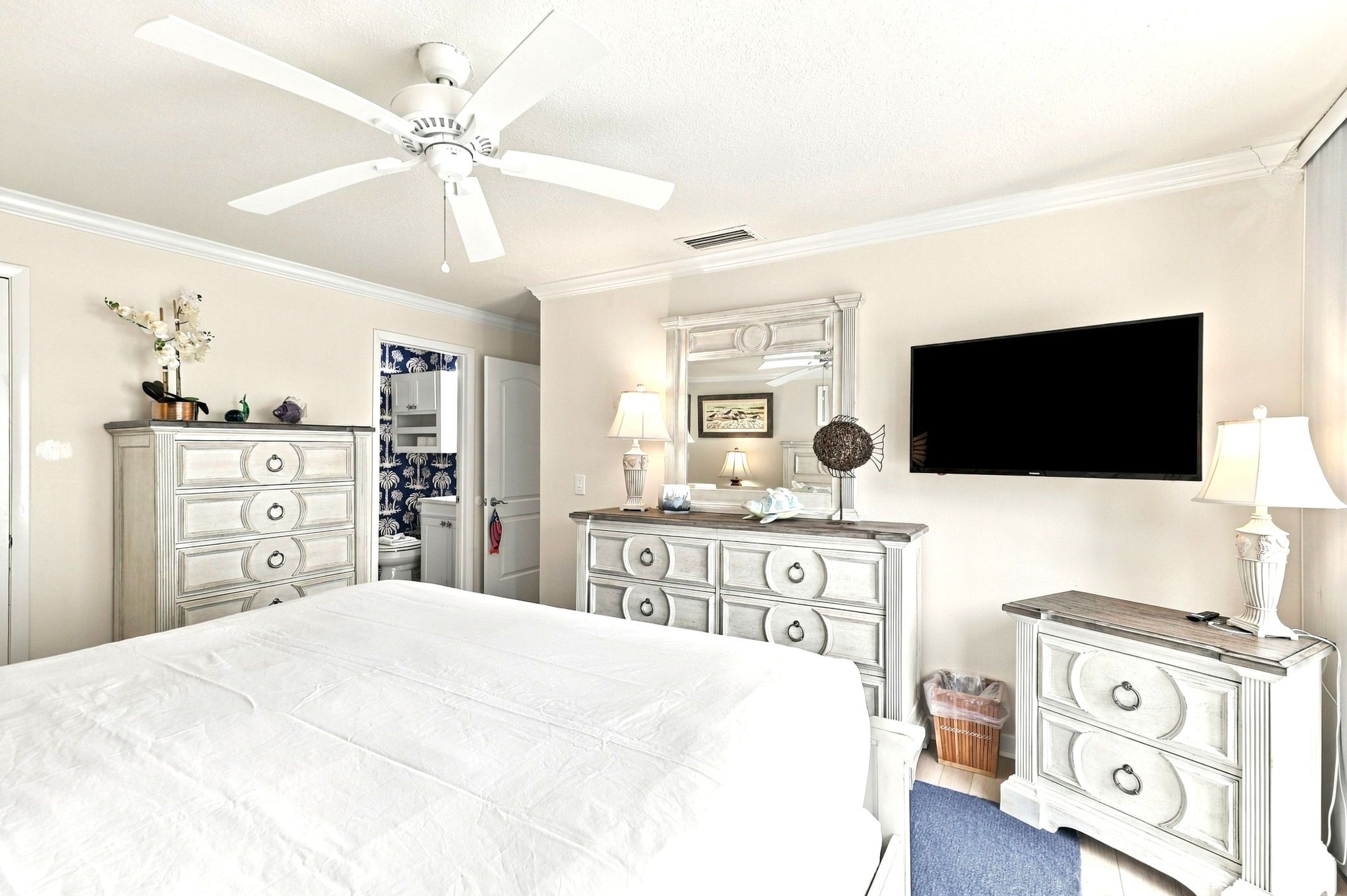 A hotel room with a large bed, a ceiling fan, a television, and a dresser with drawers.