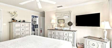 A hotel room with a large bed, a ceiling fan, a television, and a dresser with drawers.