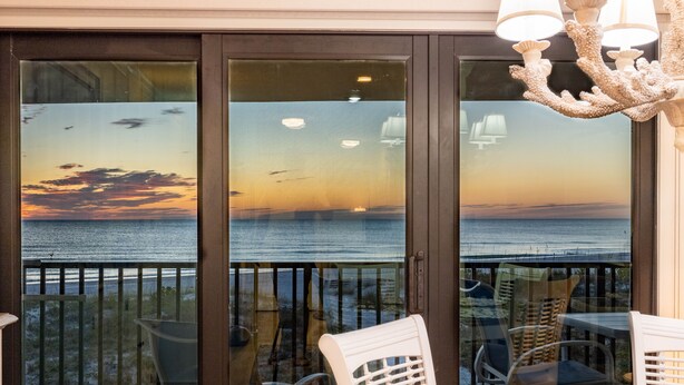 A balcony with a view of the ocean at sunset, featuring a table and chairs, and a decorative light fixture.