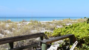 A beach view with a wooden fence and greenery in the foreground.