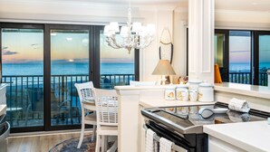 A modern kitchen with a view of the ocean, featuring a chandelier, a dining area, and a kitchen island with a stove and oven.
