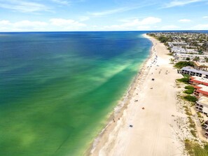 Vue aérienne d’une zone côtière avec une plage de sable et un océan bleu limpide.