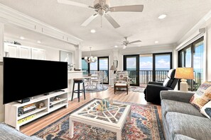 A spacious living room with a flat-screen TV, a coffee table, and a sofa. There is a balcony with a view of the ocean.