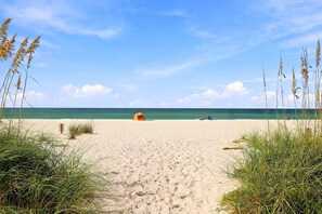 En strand med et telt og strandstole, klar himmel og hav.