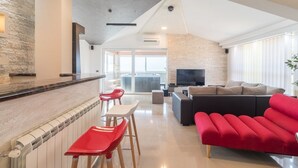 A modern living room with a red sofa, a black sectional, and a kitchen area with a stone backsplash and red bar stools. - Villa for big demands with large pool, sauna, whirlpool, fitness equipment, billiards and professional outdoor kitchen (Liznjan)