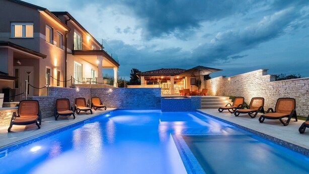 A swimming pool with lounge chairs and a stone wall. - Villa for big demands with large pool, sauna, whirlpool, fitness equipment, billiards and professional outdoor kitchen (Liznjan)