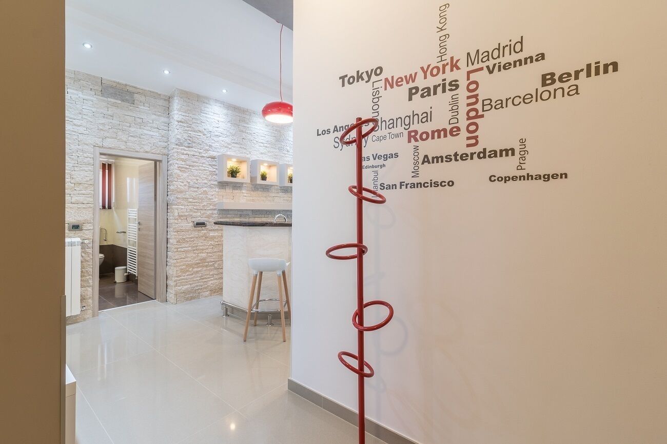 Un interno moderno con angolo cottura, una parete bianca con nomi di città e una scultura astratta rossa.