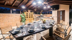 A dining area with a long table set for six, wooden chairs, a brick wall, and a ceiling fan. - Villa for big demands with large pool, sauna, whirlpool, fitness equipment, billiards and professional outdoor kitchen (Liznjan)