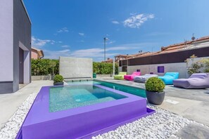 A modern outdoor pool area with a rectangular pool, surrounded by white pebbles, and furnished with colorful lounge chairs and cushions. - City finca with private heated pool, jacuzzi (Pula)