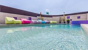 A swimming pool with colorful lounge chairs and potted plants.