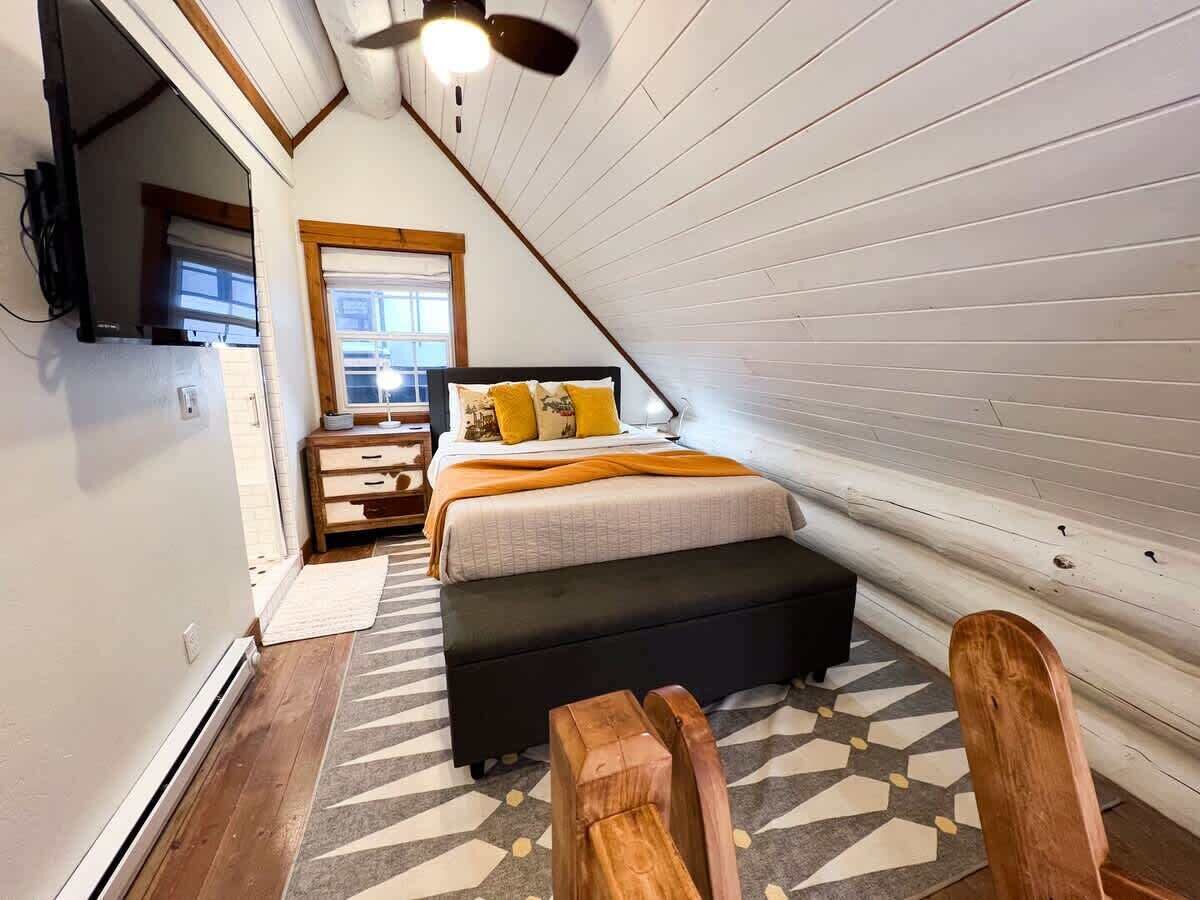 A bedroom with a bed, bedside table, lamp, and a view of the outdoors.