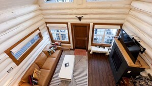 Ein rustikales Blockhaus-Interieur mit Schlafzimmer im oberen Bereich, einem Wohnbereich inklusive Sofa und Couchtisch sowie einem Kamin.
