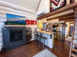 A kitchen with a fireplace, bar stools, and a large TV.