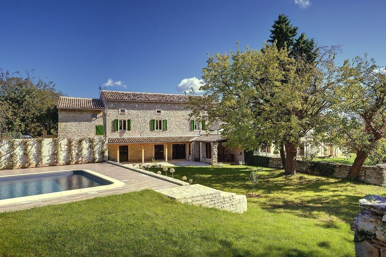 A stone house with a swimming pool, green shutters, and a well-maintained lawn.