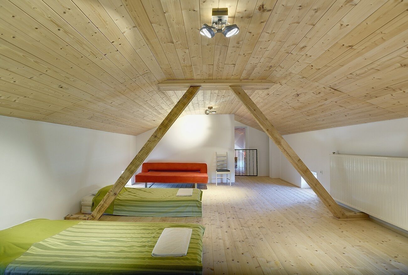 A room with a sloped ceiling, wooden beams, and a bed with green bedding.