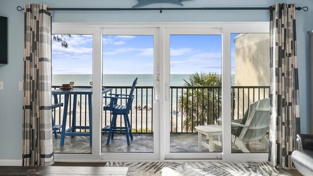 A room with a view of the beach through a sliding glass door, a ceiling shark decoration, and a patterned rug. - Sunset Terrace 201 · Gulf Front · Gulf Front (Bradenton Beach)