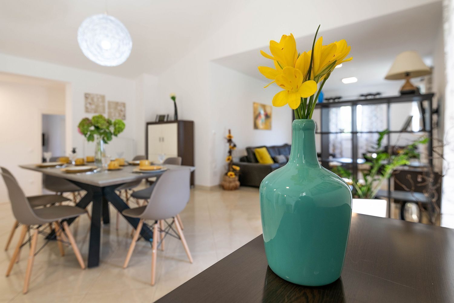 A modern dining area with a teal vase of yellow flowers on a table.