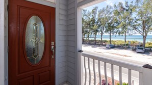 A wooden door with a glass panel and a white porch railing. - Dolphin Dance South · Gulf Views · 3-Night Min (Bradenton Beach)