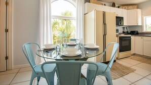 A modern kitchen with white cabinets, a glass dining table, and blue chairs. - Dolphin Dance South · Gulf Views · 3-Night Min (Bradenton Beach)