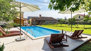 A swimming pool with a tiled deck, two lounge chairs, and a pergola with a canopy.