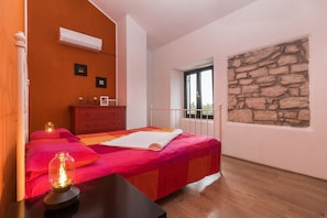 A bedroom with a bed, a dresser, an air conditioner, a stone wall, and a window. - Sunny villa with private pool and WiFi (Pula)