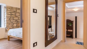 A bedroom with a bed, a stone wall, a large mirror, and a bathroom visible through an open door.