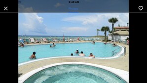 A swimming pool area with lounge chairs and a hot tub, surrounded by palm trees and a view of the ocean. - 100 PLUS 5 STARS! BEACHFRONT! FREE BEACH CHAIRS! STAND UP SHOWER! FULLY STOCKED! (Panama City Beach)
