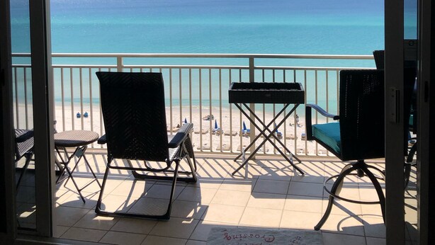 A balcony with a view of the ocean, equipped with chairs and a ceiling fan. - 100 PLUS 5 STARS! BEACHFRONT! FREE BEACH CHAIRS! STAND UP SHOWER! FULLY STOCKED! (Panama City Beach)