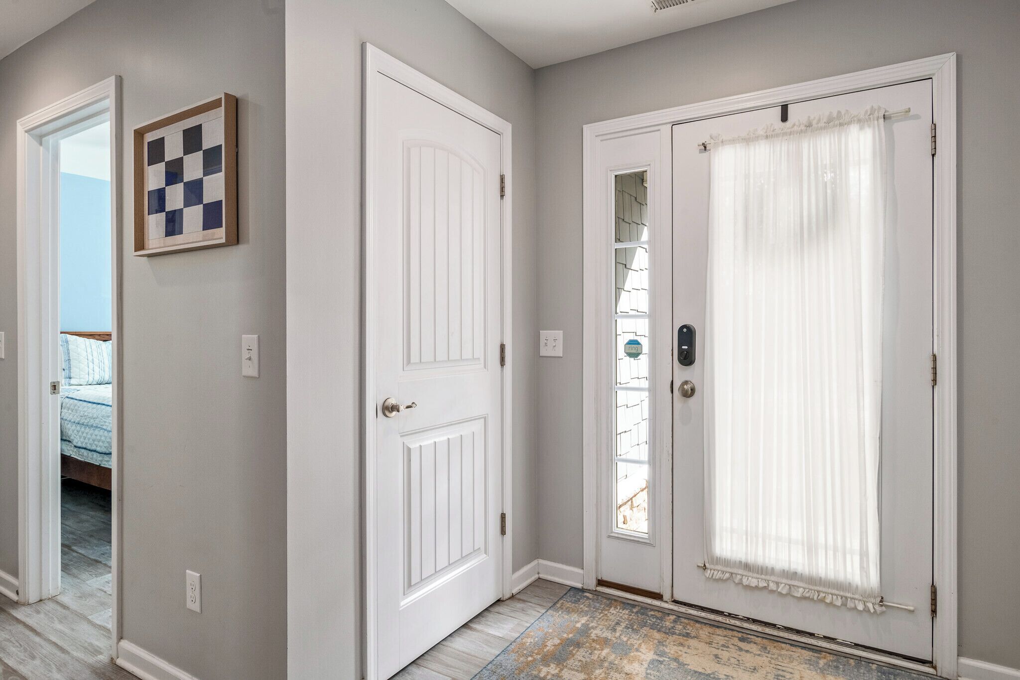 A hallway with a door leading to a bedroom, a framed artwork on the wall, and a patterned rug on the floor.