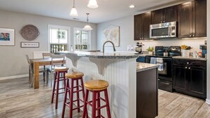 A modern kitchen with dark cabinets, a central island with stools, a microwave, and a stove. - Family oasis beach retreat in quiet woodlands (Oak Island)