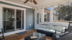 A covered patio with a sliding glass door, a wicker sofa, and a glass coffee table with glasses and a tray. - Family oasis beach retreat in quiet woodlands (Oak Island)