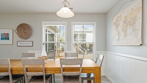 A dining area with a wooden table and chairs, a hanging light fixture, a world map on the wall, and a window with blinds. - Family oasis beach retreat in quiet woodlands (Oak Island)