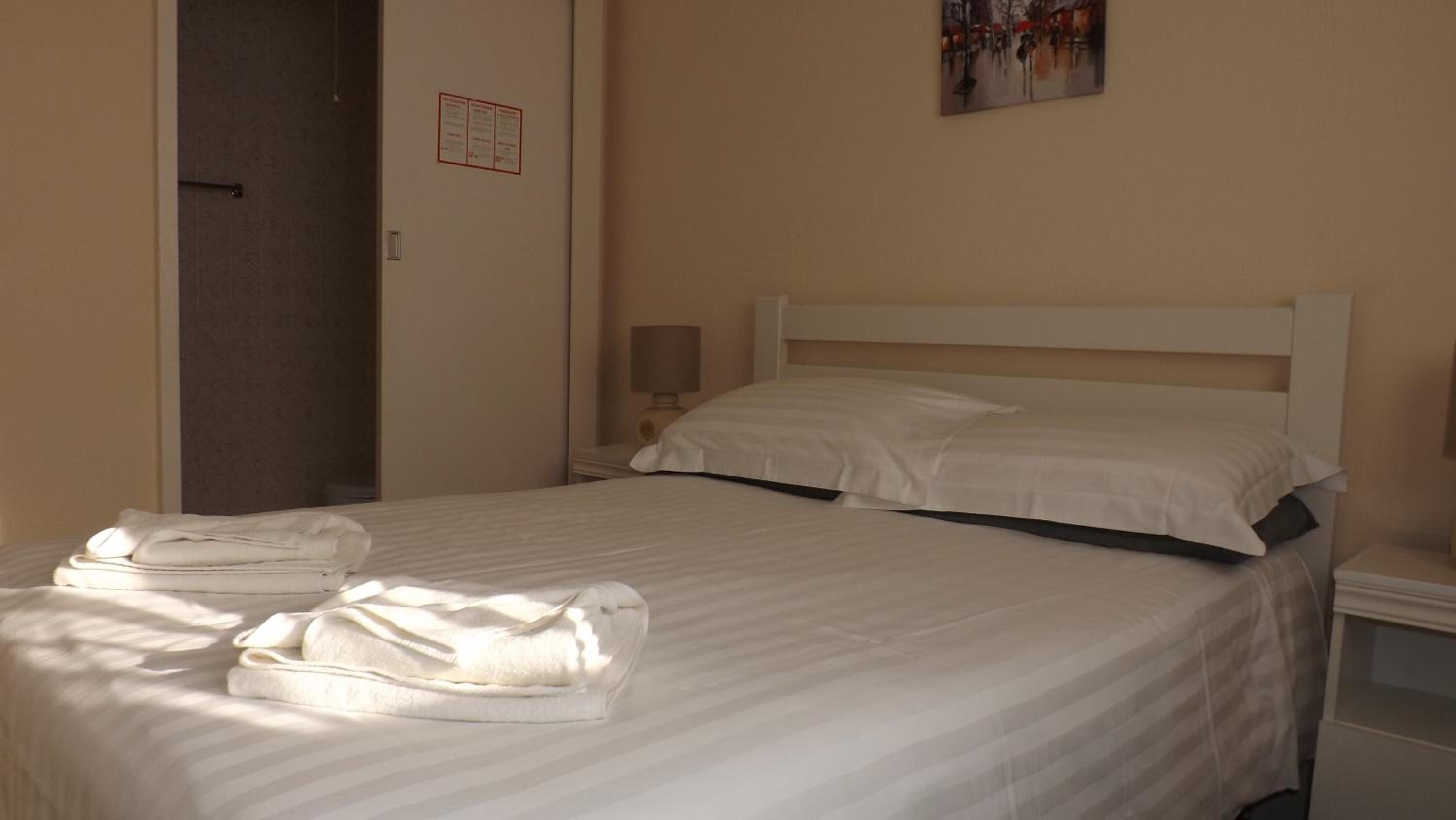 Un llit ben arrencat amb roba de llit i tovalloles blanques, una làmpada de nit i un quadre a la paret.